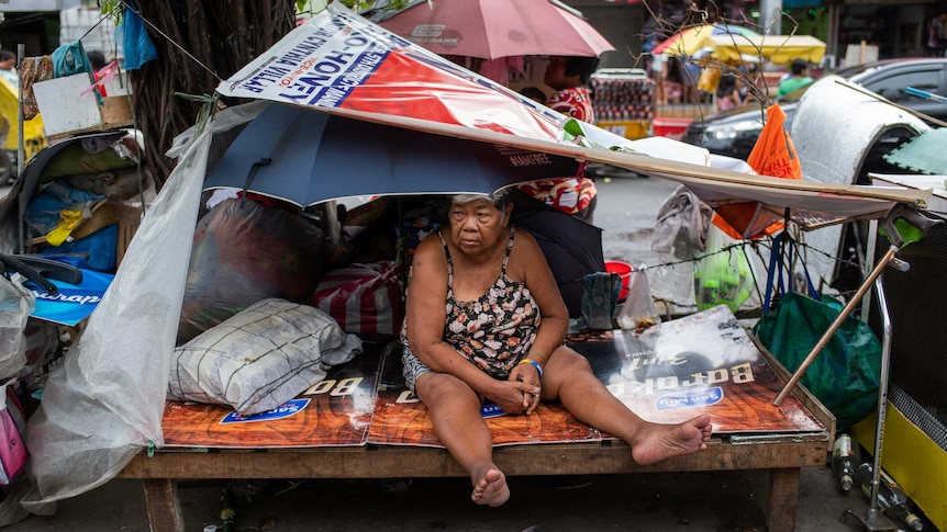 An old woman in a makeshift shelter comprised of an umbrella and political placards in the middle of a street