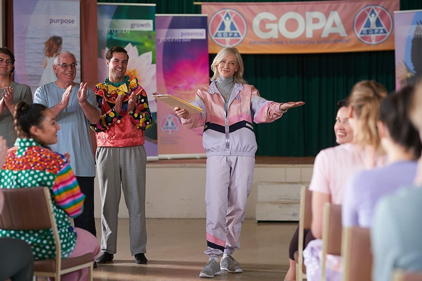 Cate Blanchett in an '80s style ski tracksuit holding a clipboard