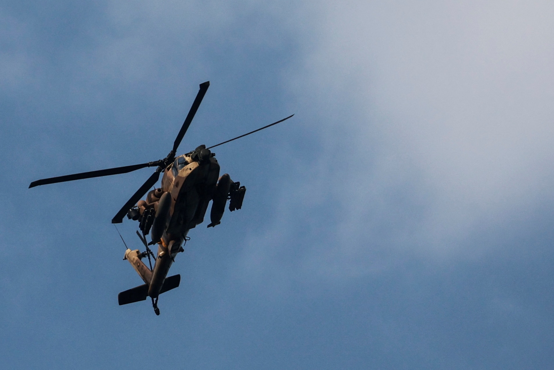 An Israeli Apache helicopter loaded with missiles flies through clear blue sky.