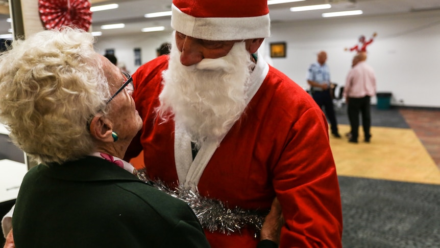 Prisoner dressed up as Santa giving an elderly citizen a hug.