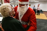 Prisoner dressed up as Santa giving an elderly citizen a hug.