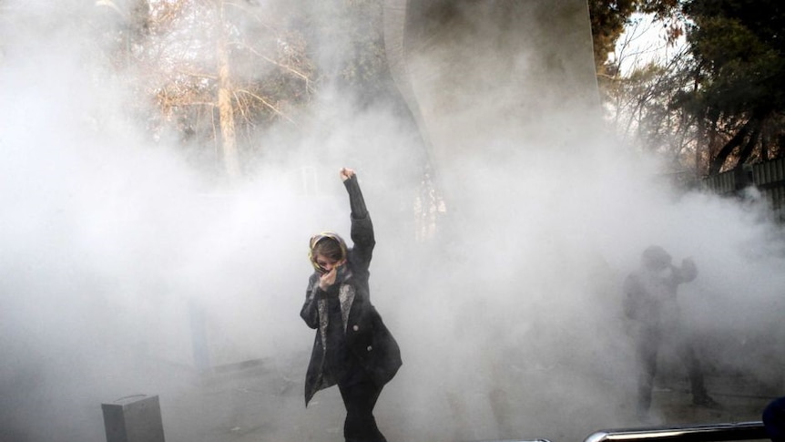 A university student attends a protest inside Tehran University while a smoke grenade is thrown by anti-riot Iranian police.
