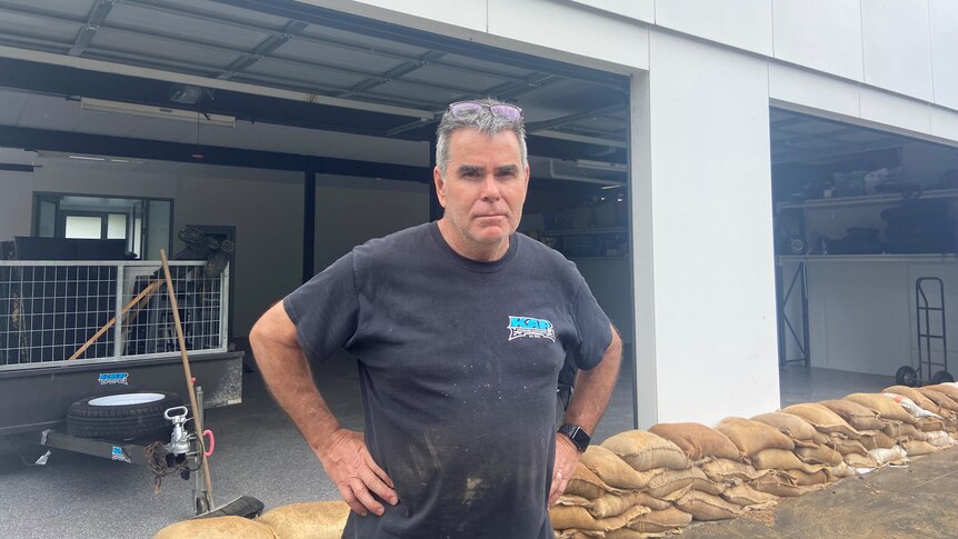 A man standing with hands on hips infront of sandbags, protecting an open garage 