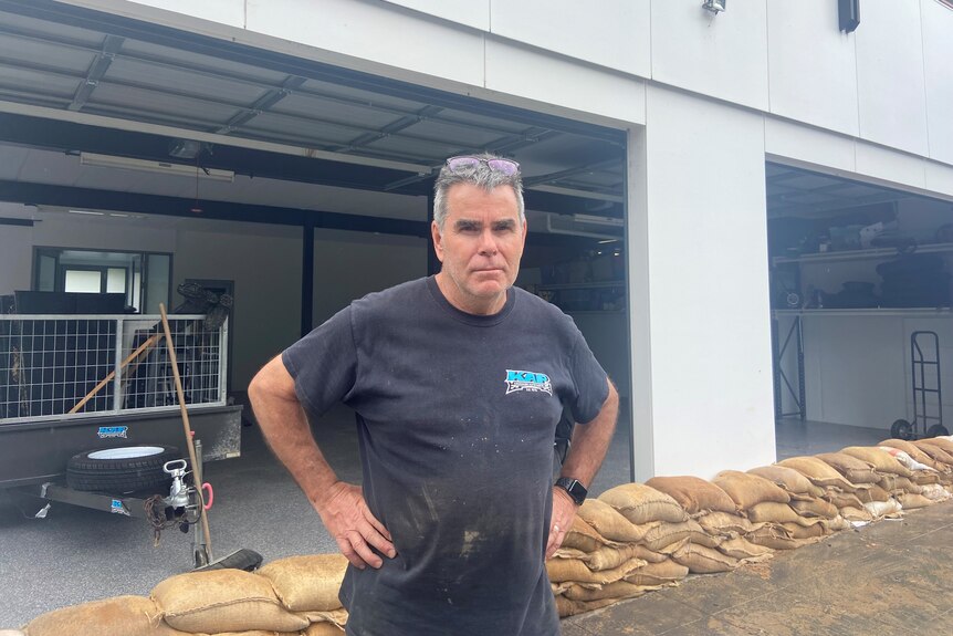 A man standing with hands on hips infront of sandbags, protecting an open garage 