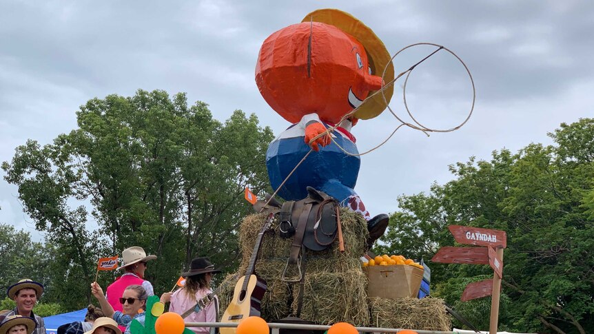 The Gayndah Orange festival mascot, a large orange with a hat, sits on a float leading the festival parade