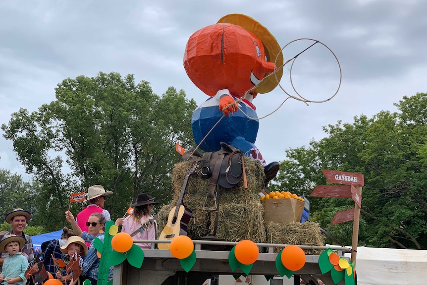 The Gayndah Orange festival mascot, a large orange with a hat, sits on a float leading the festival parade