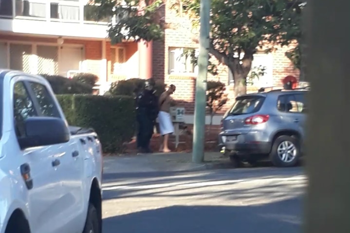 A shirtless man is arrested outside a unit block.