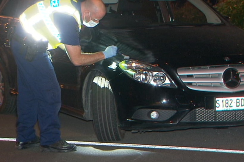 A police officer dusts a black car with a soft brush
