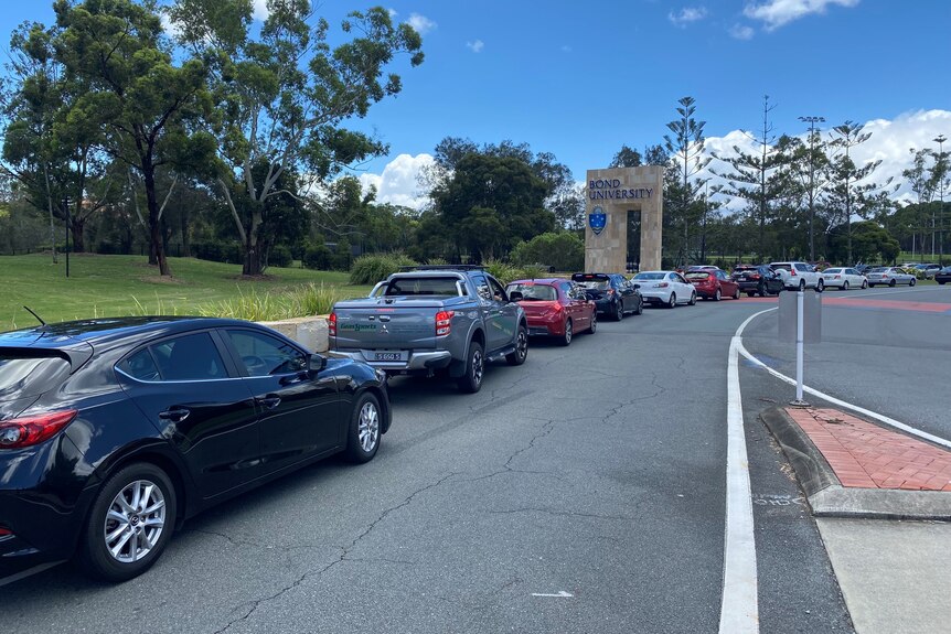 A long line of cars with the Bond University sign in background.
