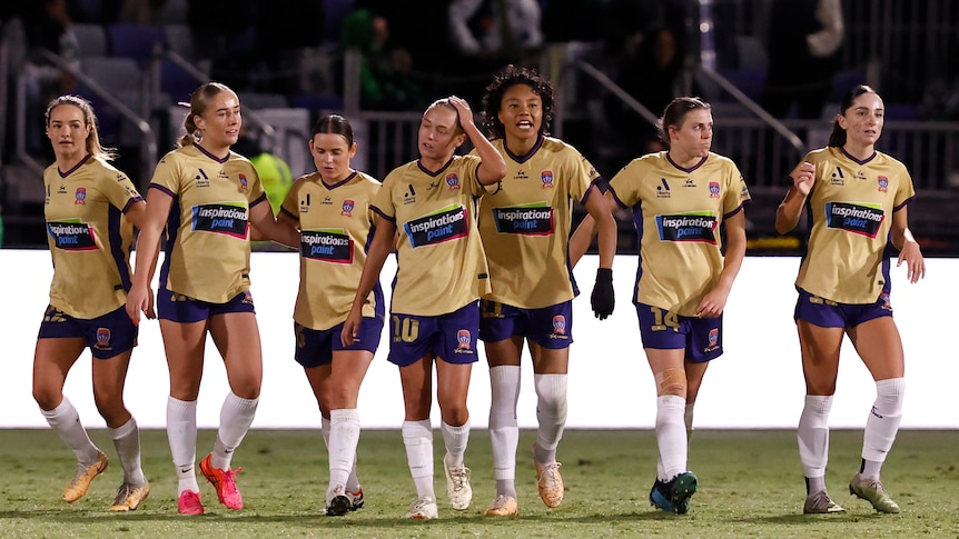 A women's soccer team wearing gold and blue celebrate scoring a goal in a big game