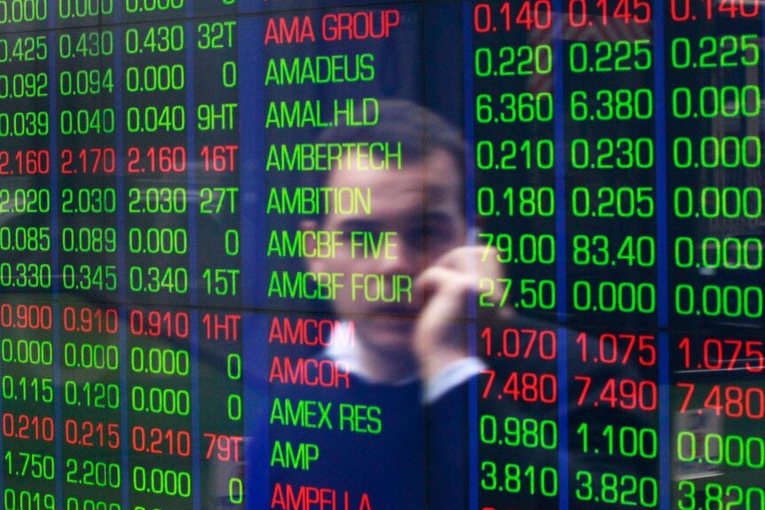 An office worker is reflected in a stock board at the ASX while he talks on the phone.