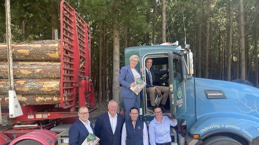 A group of seven people, including the SA Premier, stand next to an electric B double truck loaded with logs.