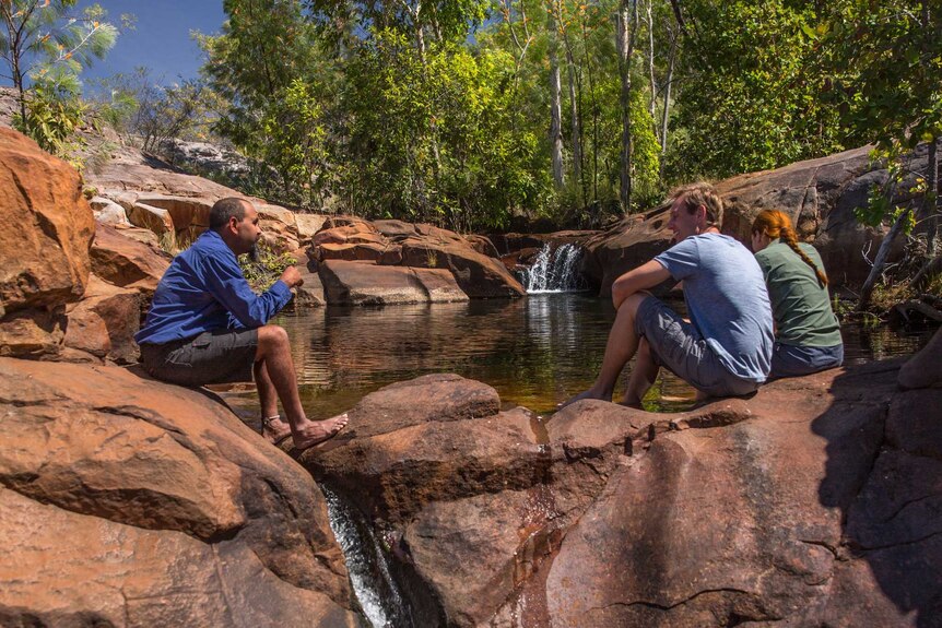 Jamie Brooks sits with two tourists near a waterfall