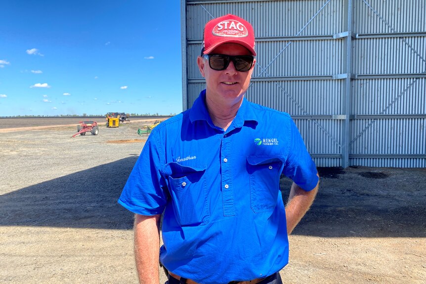 Man in blue workshirt and red cap wearing sunglasses.