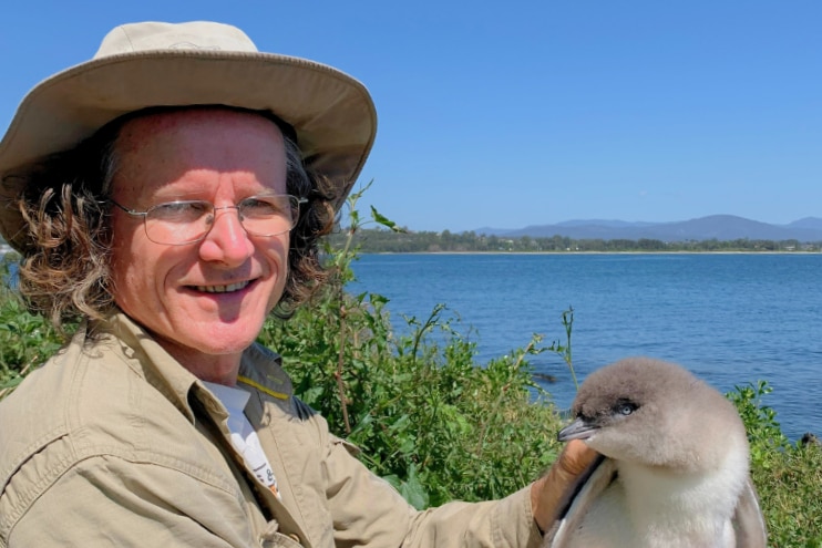 A man holding a little penguin with water in the background