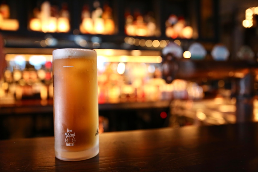 A close up of a frosty beer sitting on top of a counter at a bar