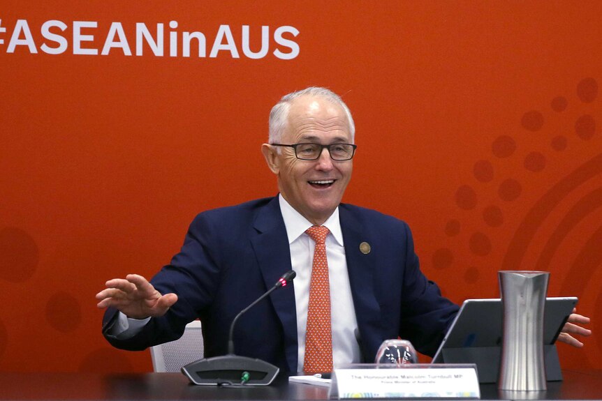 Malcolm Turnbull seated at desk, smiling while addressing summit.