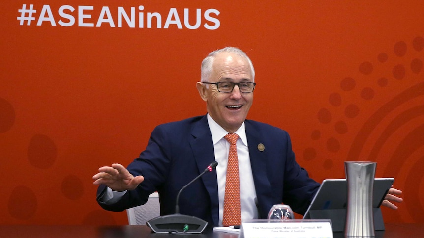 Malcolm Turnbull seated at desk, smiling while addressing summit.