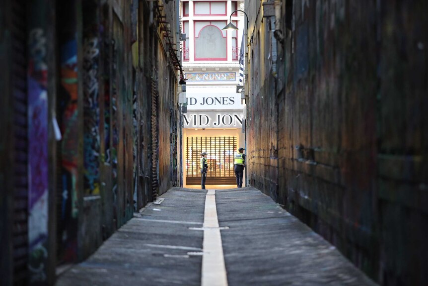 A long view of a Melbourne laneway plastered with posters and graffiti, with two police and the David Jones shopfront at the end