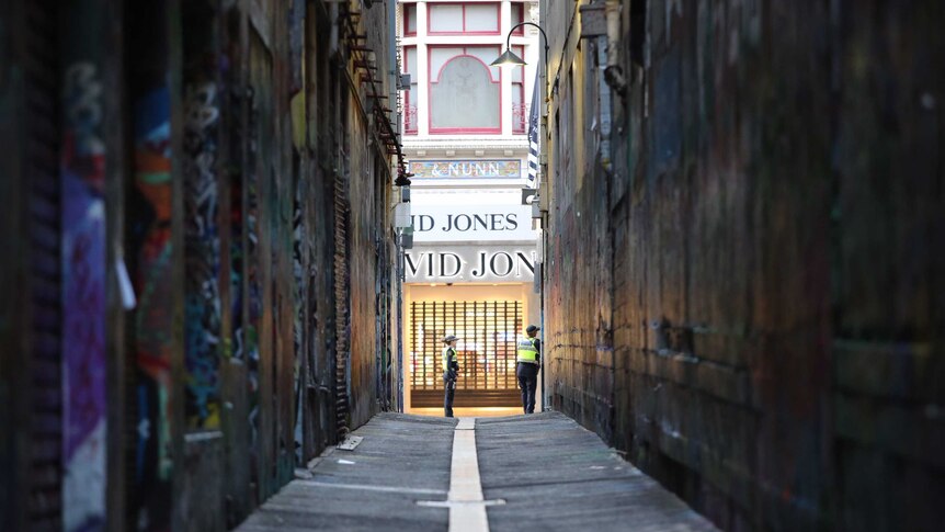A long view of a Melbourne laneway plastered with posters and graffiti, with two police and the David Jones shopfront at the end