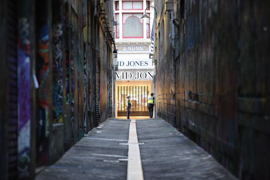 A long view of a Melbourne laneway plastered with posters and graffiti, with two police and the David Jones shopfront at the end