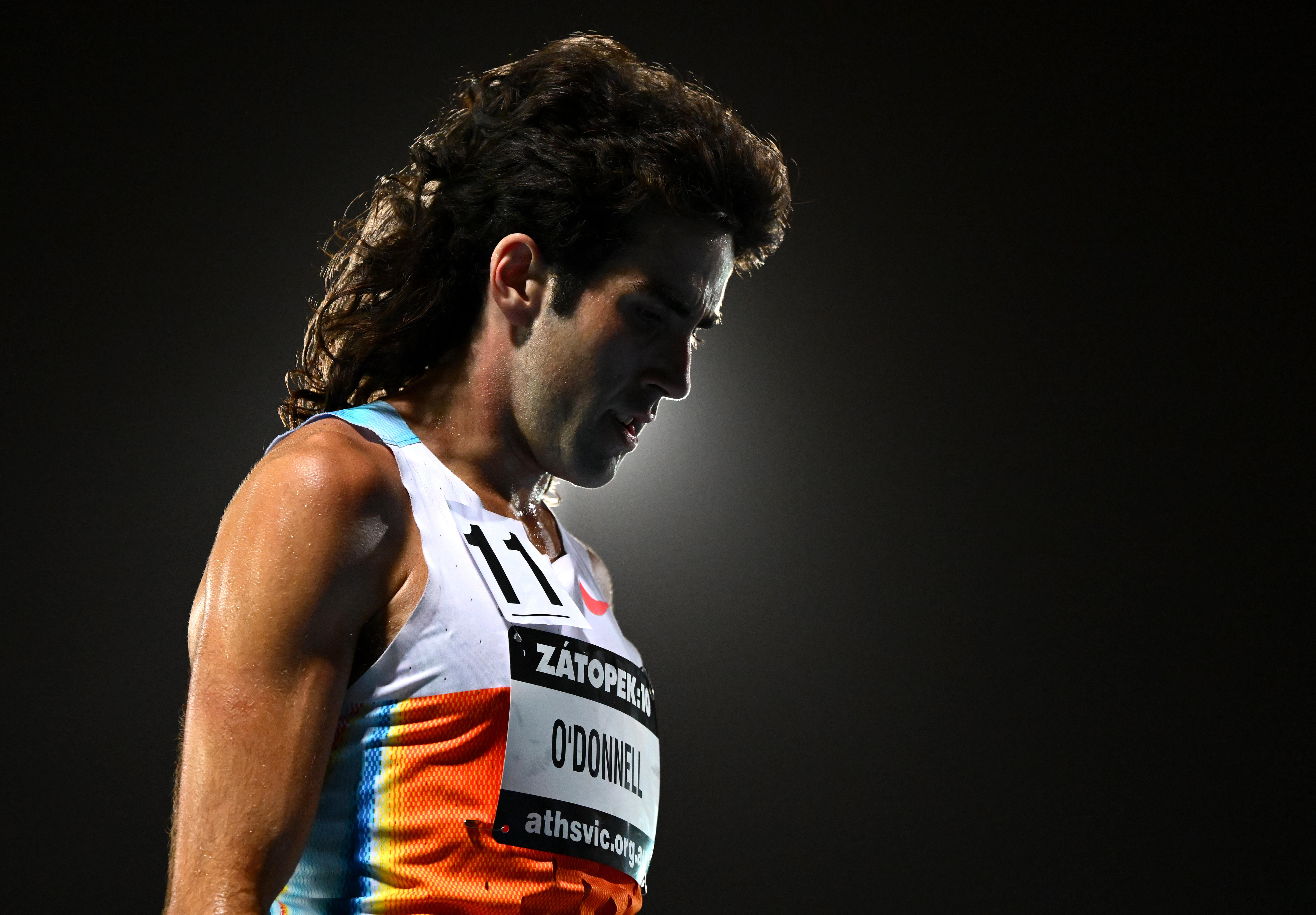 Seth O'Donnell stands on an athletics track with a light behind his mullet.