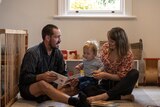 A young couple sit on the floor with their baby son and read a book Dear Zoo
