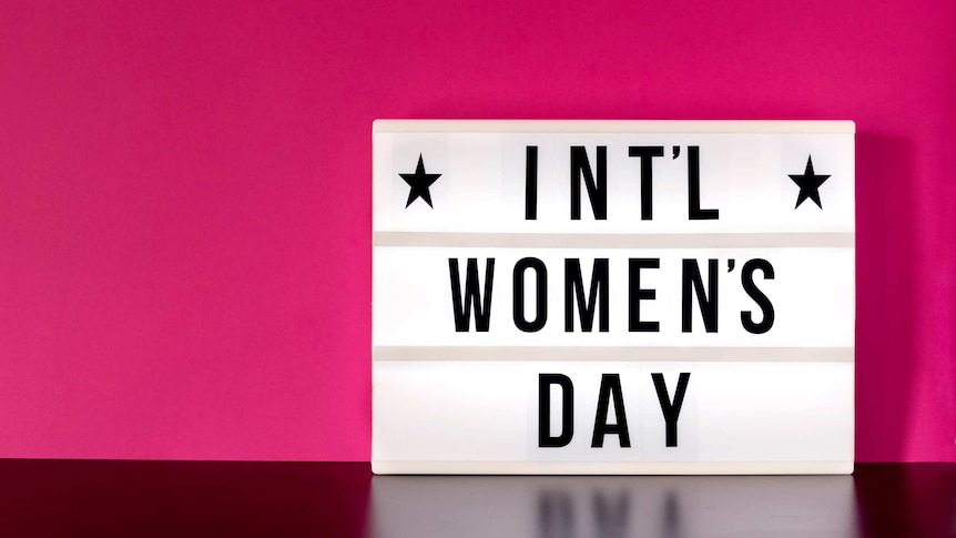 Close-up of an International Women's Day sign, against a plain pink background.