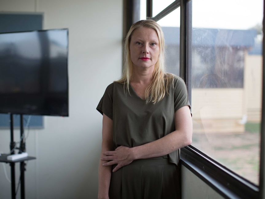 Agata stands next to a classroom portable window with a concerned expression.