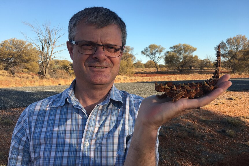Man with a thorny devil in his hand in an arid setting.