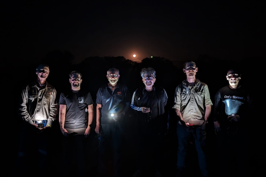 line of men at night with faces lit by torches 