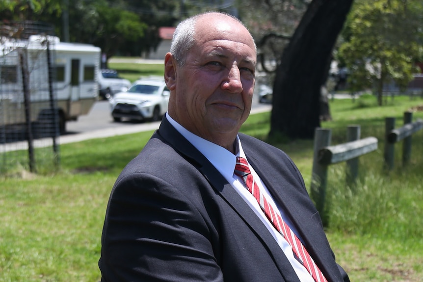 A man in a suit and tie sits on a park bench. 