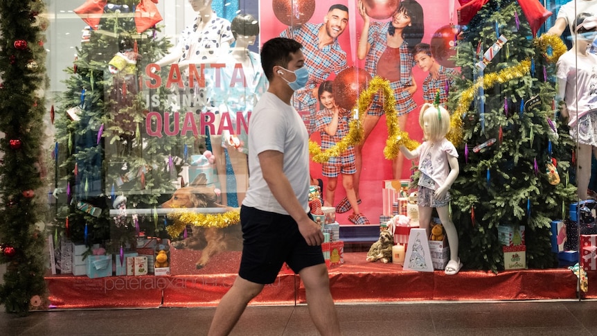 A man wearing a mask walks past a shop's Christmas-themed window display.