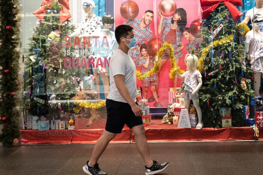 A man wearing a mask walks past a shop's Christmas-themed window display.