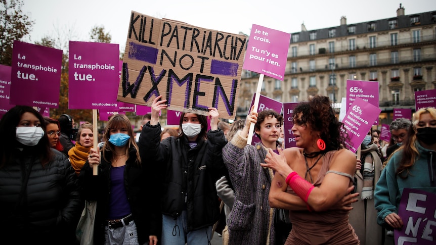 Women hold up pink placards and banners at a protest for women's rights in Paris.