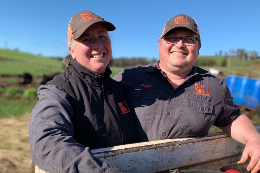 A man and woman stand side by side wearing blue and orange caps and shirts, smiling.