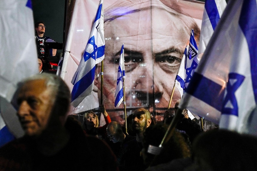 A large image of Netayahu's face, partially obscured by flags and protesters