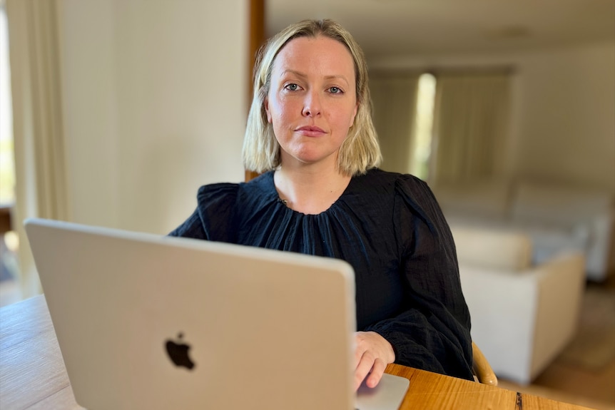 Stephanie Wescott wears a black top and sits at a dining room table on a silver laptop.
