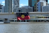 A large Aboriginal flag hanging from Brisbane's Victoria Bridge over the river with the words "vote no" written across it