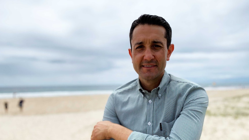 Man at beach, cross armed, smiling.