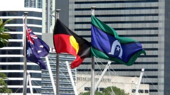 Three flags billow in the wind in front of skyscrapers