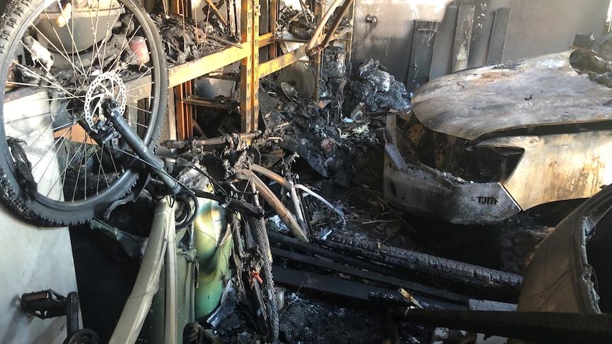 The charred remains of an electric bike and a car after fire swept through a garage. 