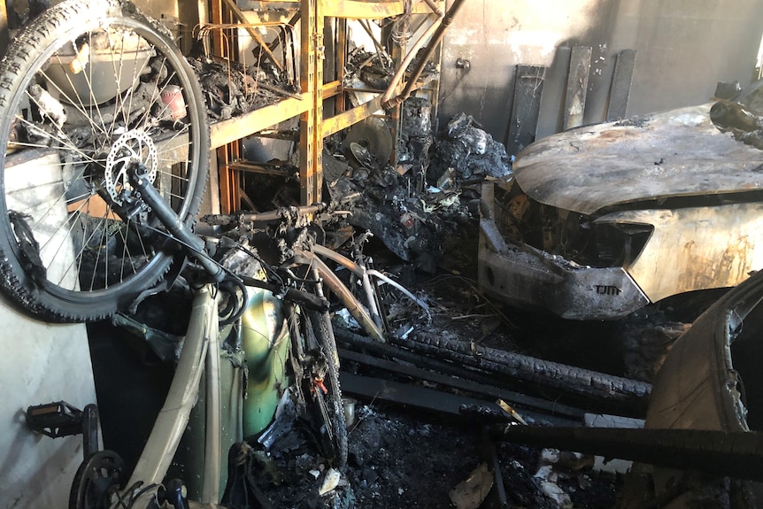 The charred remains of an electric bike and a car after fire swept through a garage. 