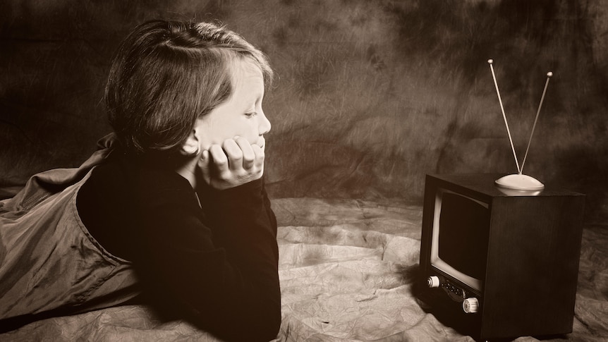 black and white vintage photo of a child looking at a small television box