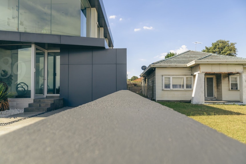 A photograph of a new multi-storey apartment building and an old weatherboard house, viewed from the street.