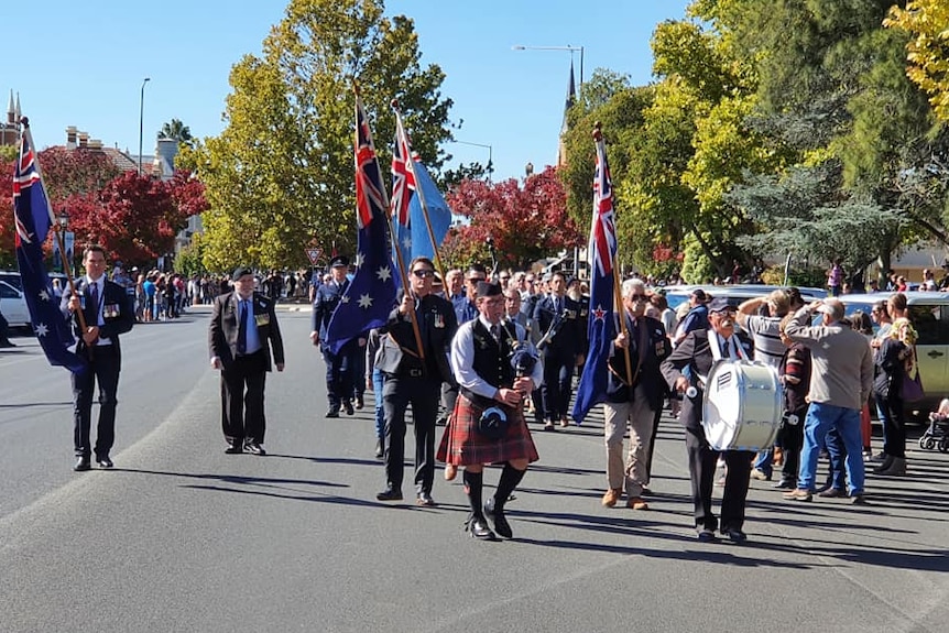 Large group of people marching for Anzac day with Australian flags.
