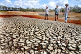 Three men stand on the bank of an almost dry dam