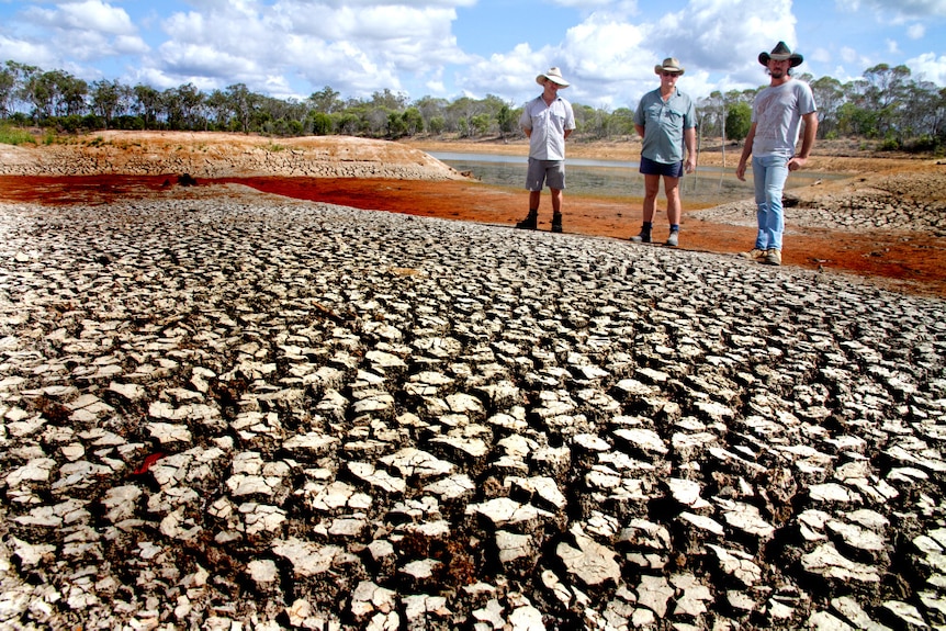 Three men stand on the bank of an almost dry dam