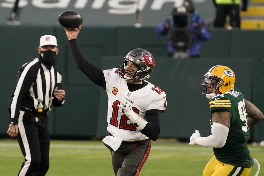 An NFL quarterback releases the ball downfield as an umpire and opposition defender look on.
