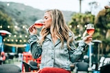 Young woman holding two glasses of wine and drinking from one for a story about the dangers of casual alcohol drinking.